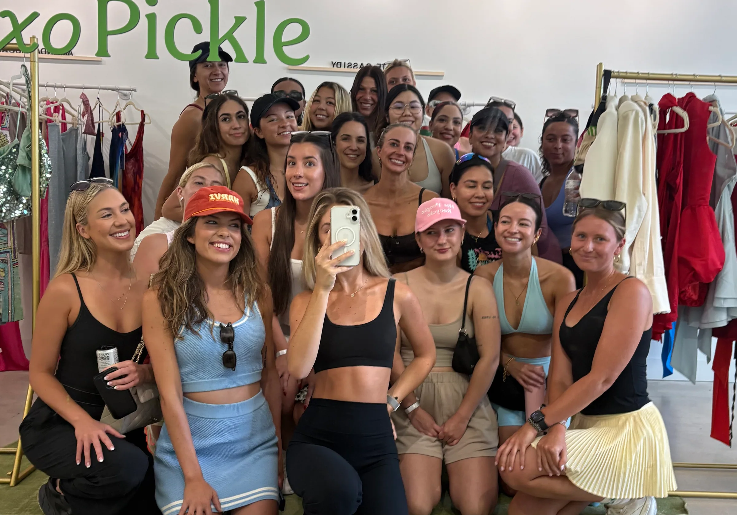 A large group of women smiling for a mirror photo inside a clothing shop.