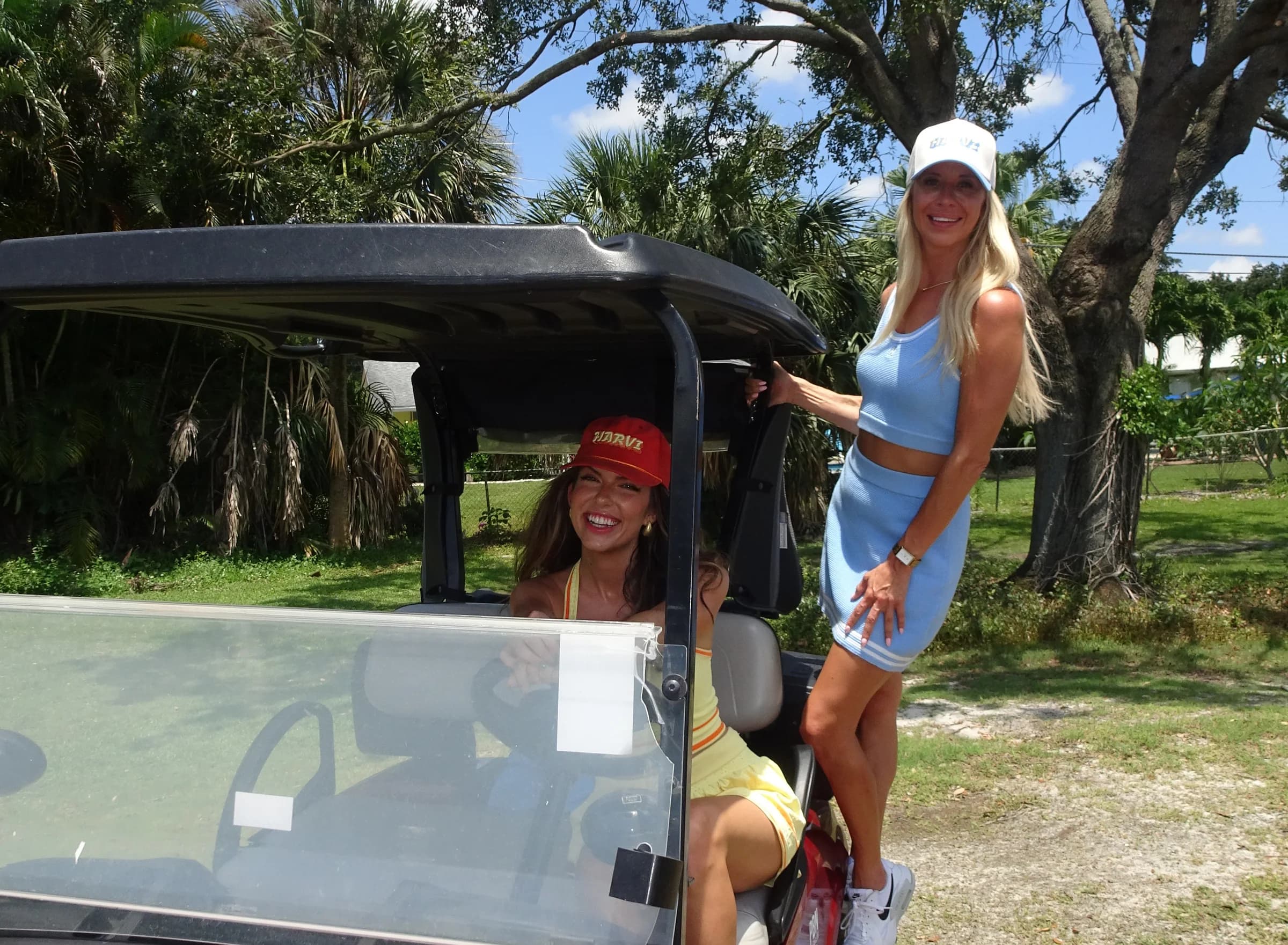 Two women in colorful athletic outfits posing together beside a golf cart outdoors.